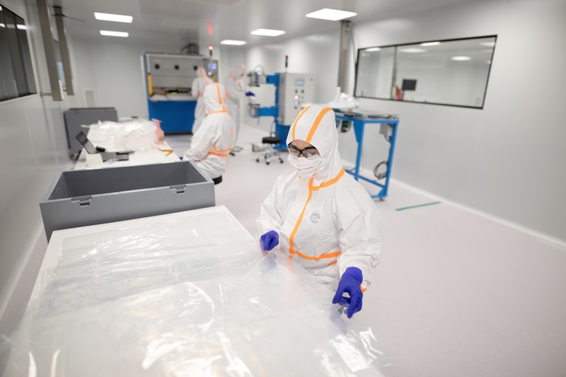 Workers in cleanroom suits handling materials in a semiconductor fabrication facility