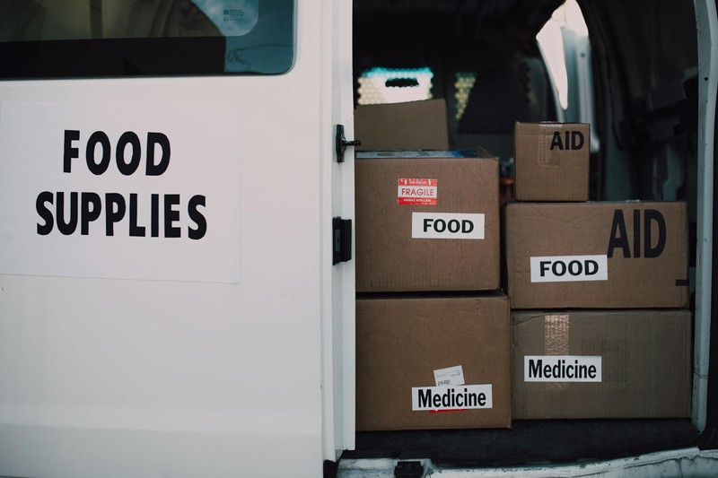 Stacked cardboard boxes labeled FOOD, AID, and Medicine inside a white delivery van