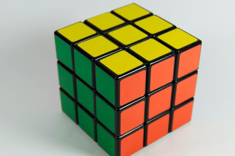 A solved Rubik's Cube showing yellow, orange, and green faces against a white background