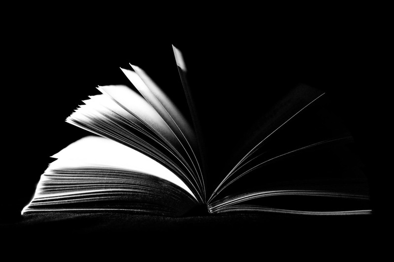 An open book with fanned pages against a dark background in black and white