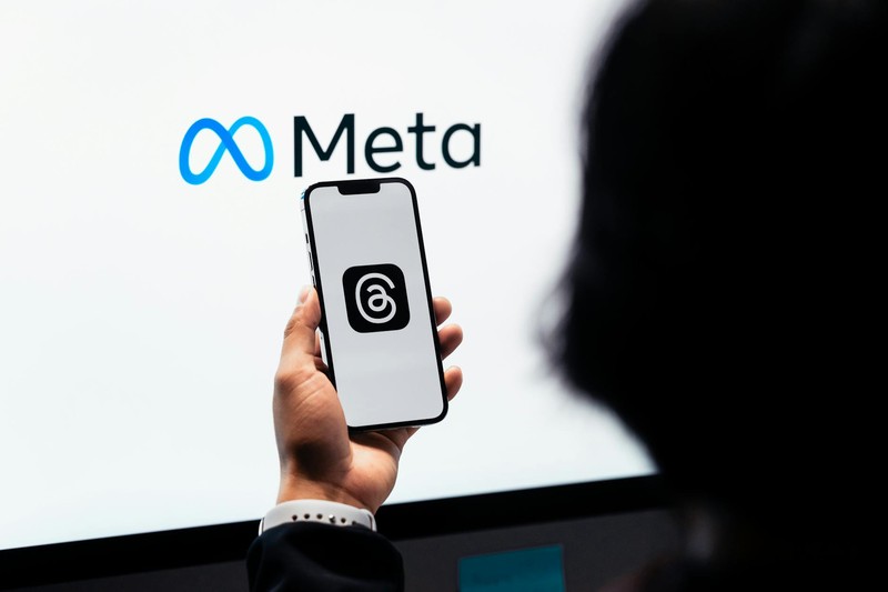 A hand holds a smartphone showing a Meta app with the Meta logo displayed in the background