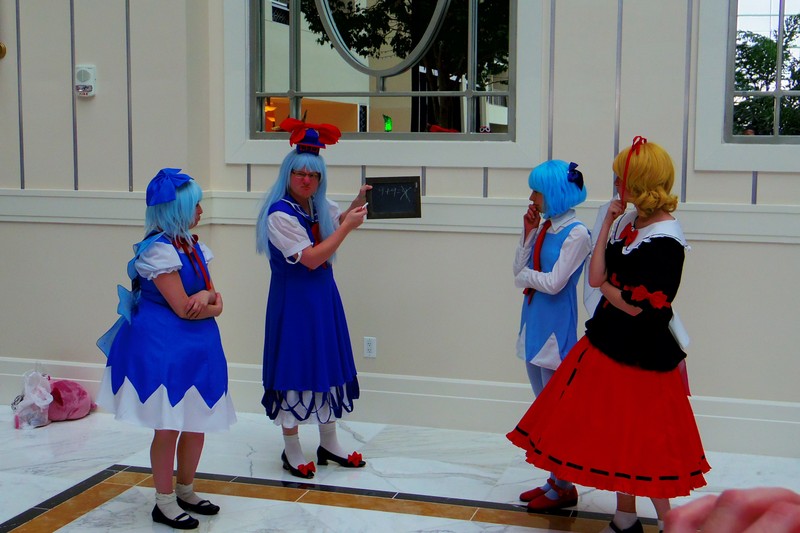 Touhou cosplayers at a convention, including a Keine Kamishirasawa cosplayer with two Cirno cosplayers and a Medicine Melancholy cosplayer