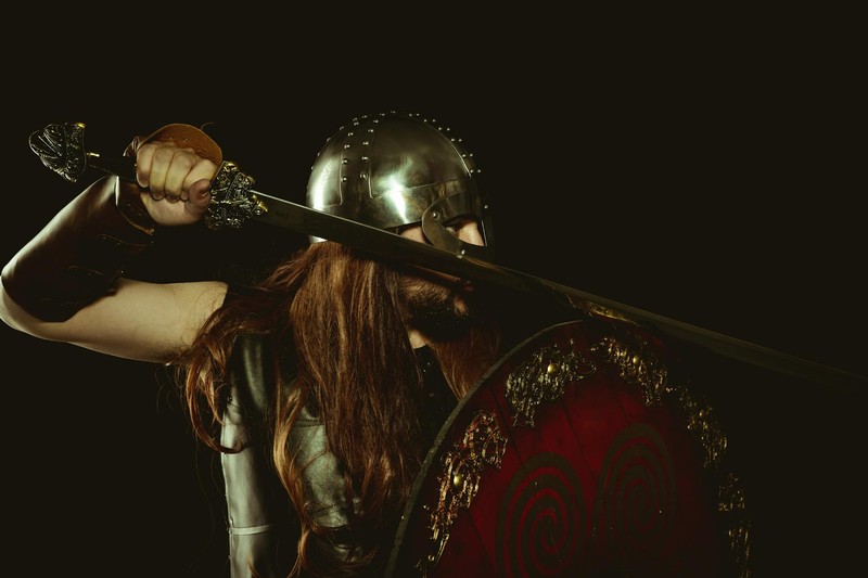 A medieval warrior in armor holding a sword and shield against a dark background