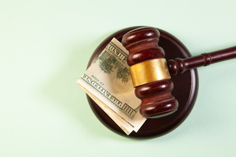 A wooden gavel resting on a stack of US currency on a green background