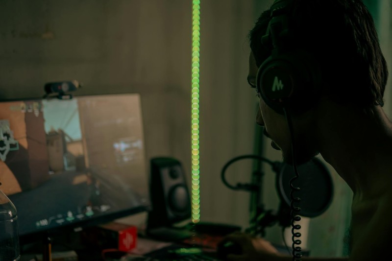 A focused gamer wearing a headset plays a video game on a desktop computer in a dimly lit room