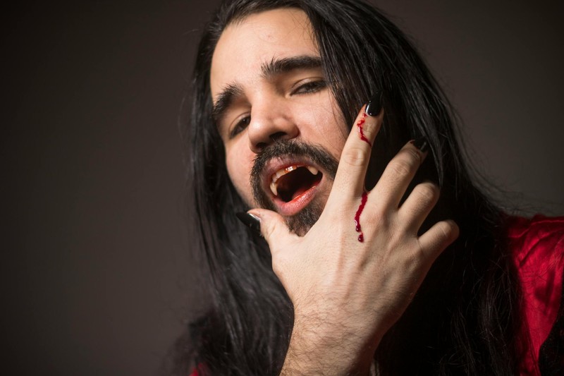 A man in vampire cosplay with fangs and blood on his fingers against a dark background