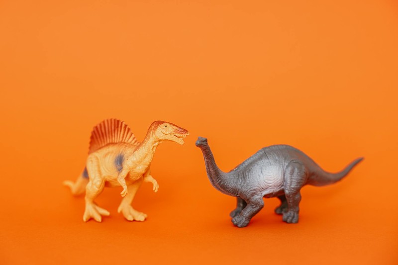 Two plastic toy dinosaur figurines facing each other on a bright orange background