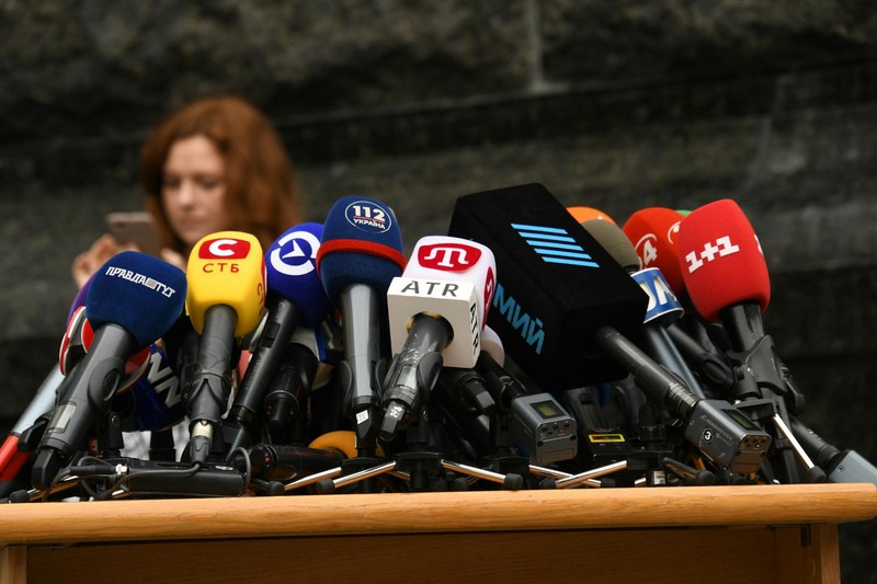 Multiple press microphones clustered on a podium at a press conference in Kyiv, Ukraine