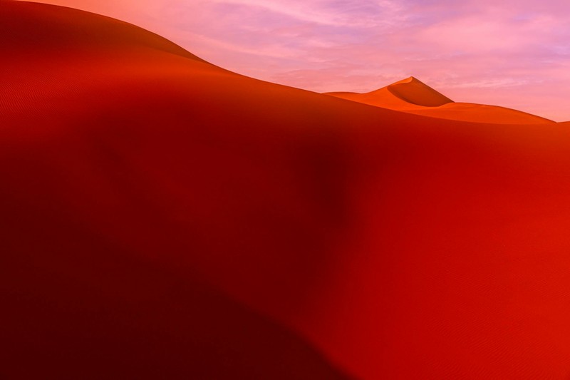Crimson red sand dunes stretching to the horizon under a soft pink sky at sunset