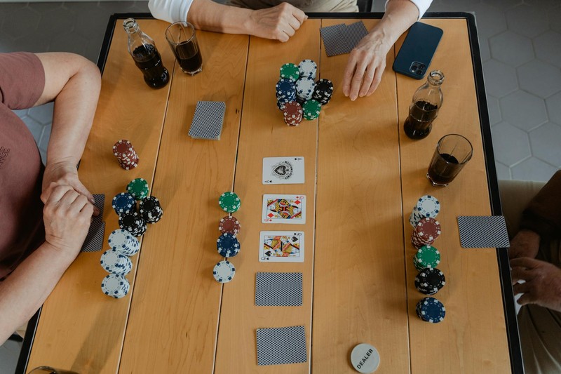 A casual poker game with chips, cards, and drinks on a wooden table, with friends' hands visible around the table