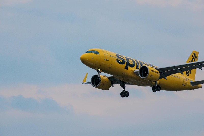 A bright yellow Spirit Airlines jet in flight with landing gear extended against a clear blue sky