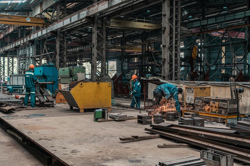 Industrial workers welding and operating machinery in a metal workshop