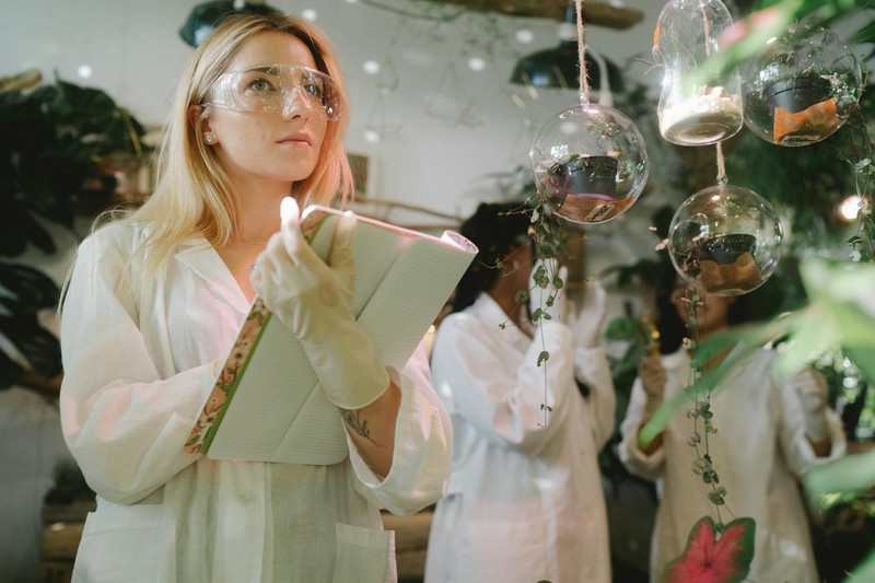 Female scientist examining plant specimens in a laboratory with hanging glass globes containing plant samples