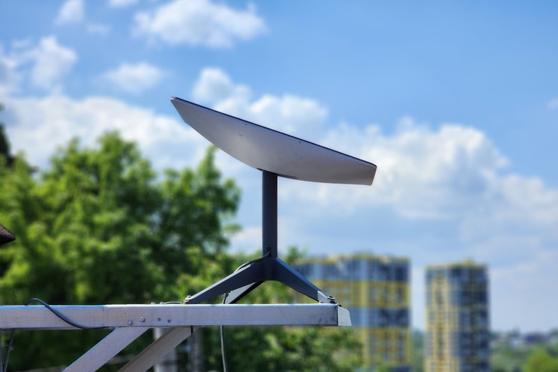 A Starlink satellite terminal mounted outdoors against a blurred sky and treetop background