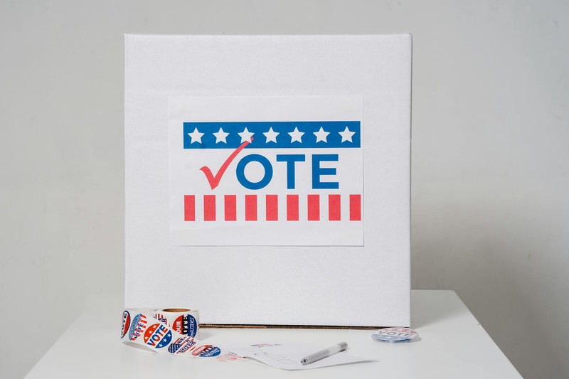 White ballot box with patriotic VOTE sign and I VOTED stickers on a table