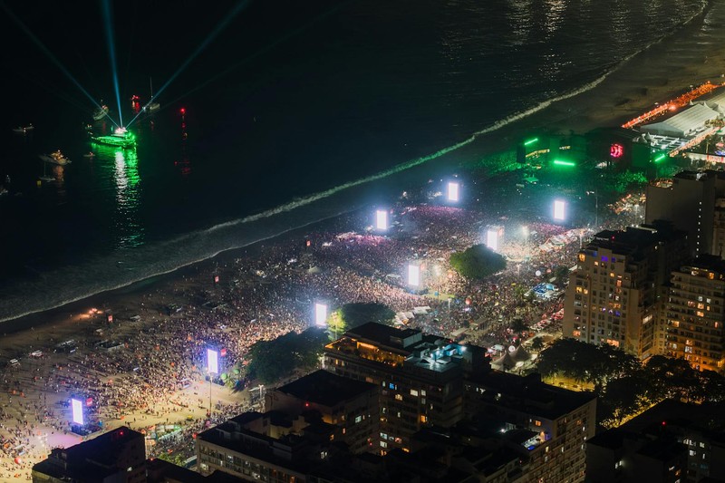 Aerial night view of Copacabana Beach in Rio de Janeiro packed with a massive crowd and illuminated stages during a large-scale celebration