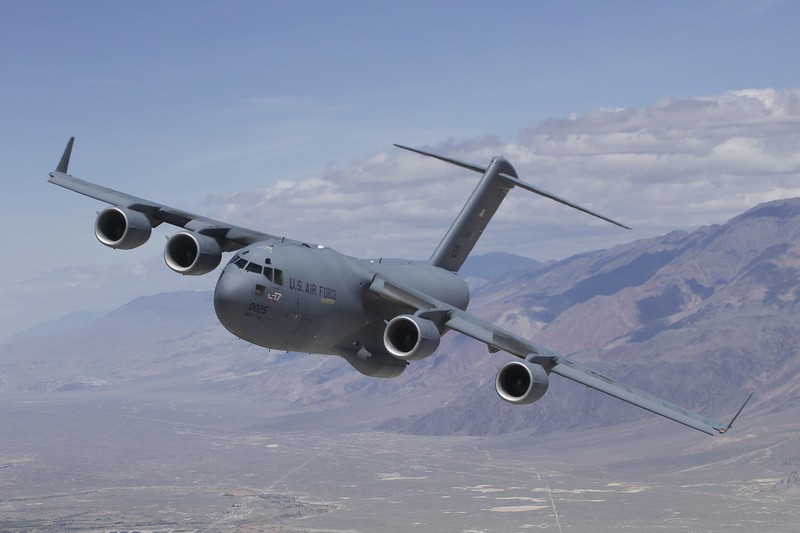 A U.S. Air Force C-17 Globemaster III military transport aircraft in flight over a mountainous landscape