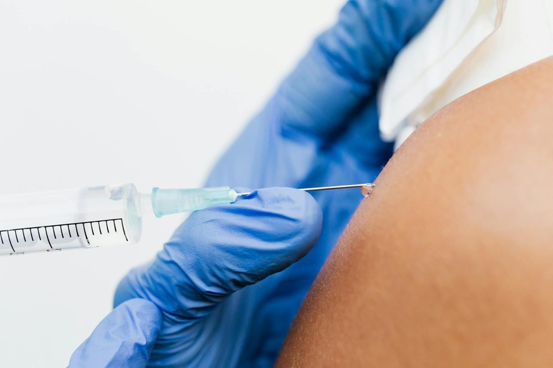 A healthcare professional in blue gloves administers an injection with a syringe