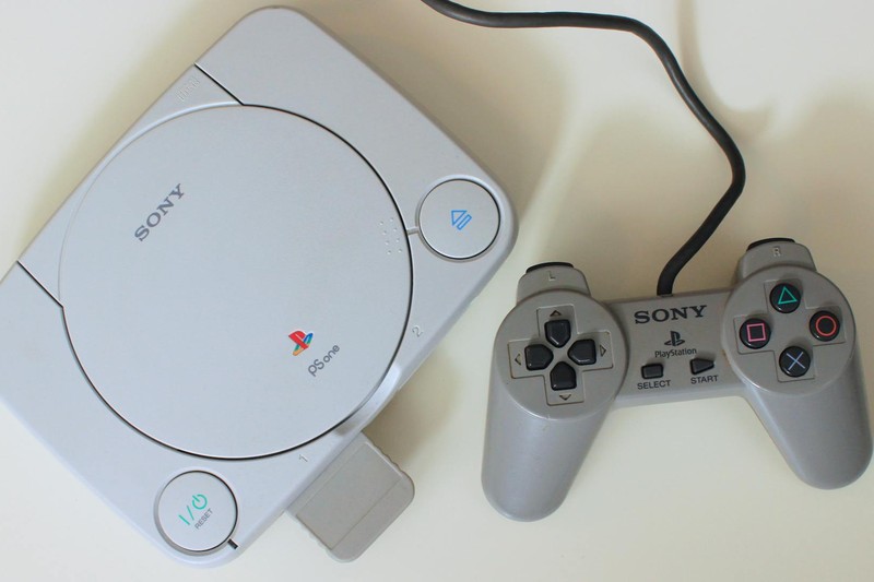 A retro Sony PlayStation One console with its original controller on a light background