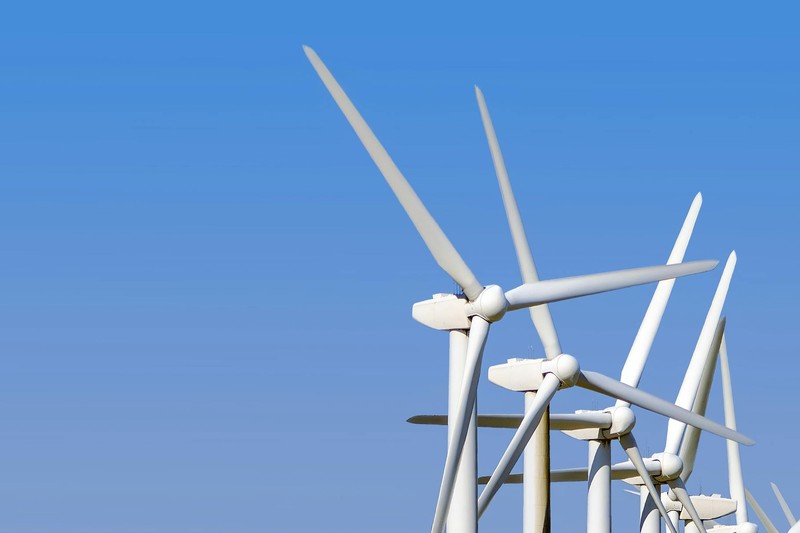 Multiple white wind turbines standing tall against a clear blue sky, viewed from a low angle
