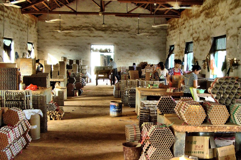 Interior of a fireworks workshop in Liuyang, China, showing workers and stacked firework tubes