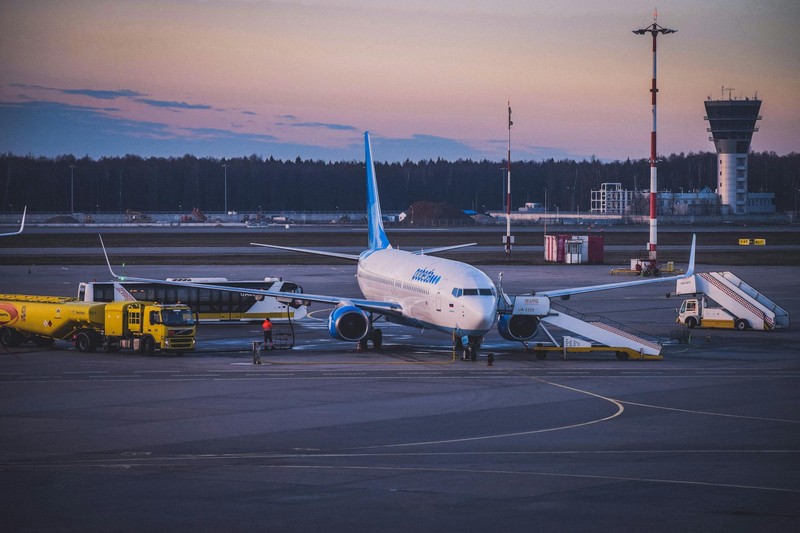 Commercial jet airplane parked on airport tarmac at twilight with ground support vehicles and boarding stairs