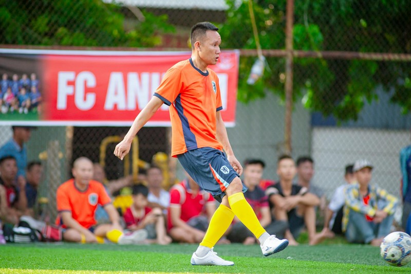 A soccer player in an orange jersey kicks the ball during a match watched by spectators