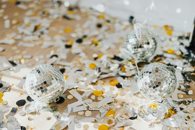 Disco balls surrounded by metallic confetti on a table