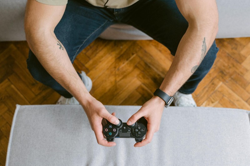 Hands holding a black game controller during a gaming session in a living room