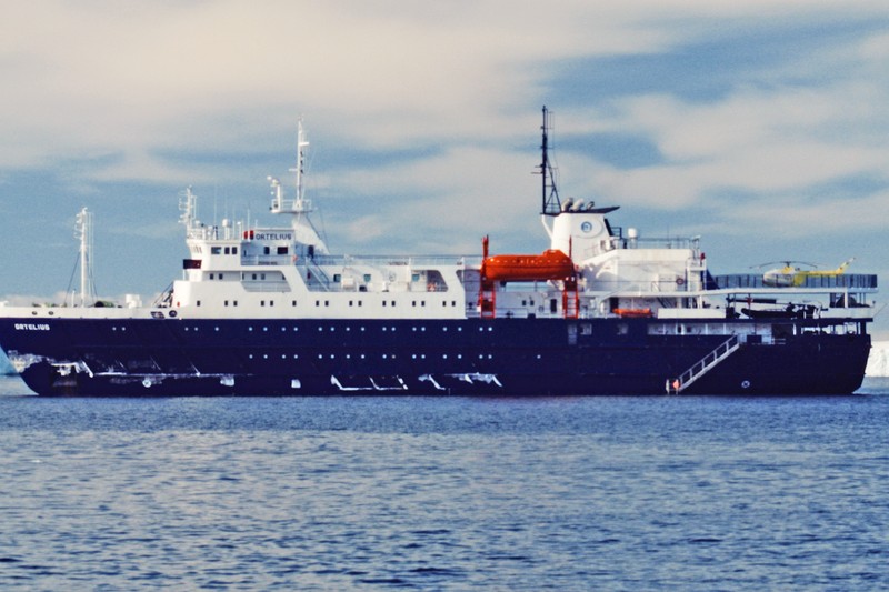 The expedition vessel MV Ortelius sails on calm open ocean under partly cloudy skies.