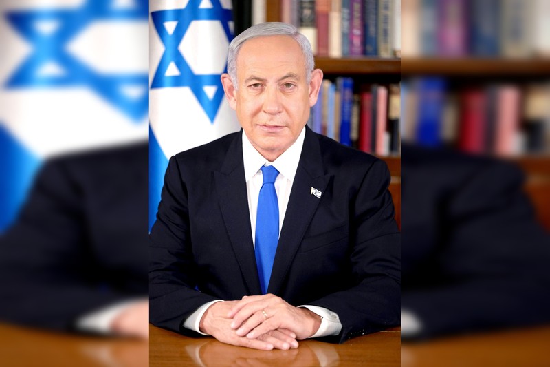 Official portrait of Israeli Prime Minister Benjamin Netanyahu in his office with the Israeli flag visible in the background.