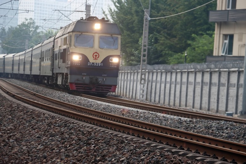 A passenger train traveling on tracks through an urban area with buildings in the background
