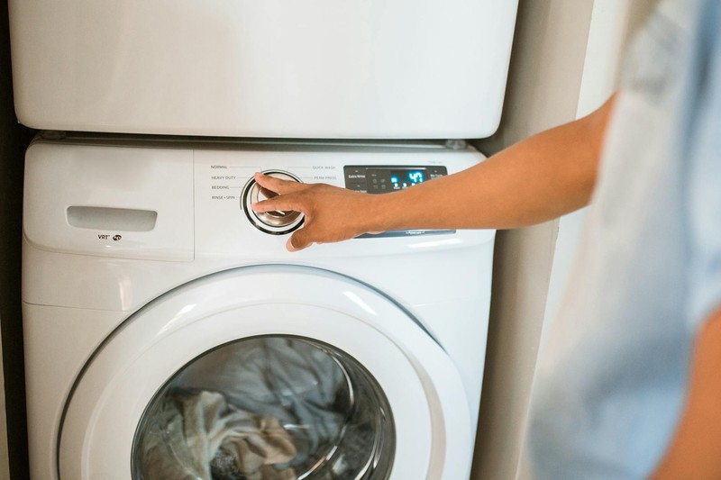 A person's hand adjusts the settings on a modern front-loading washing machine in a laundry room
