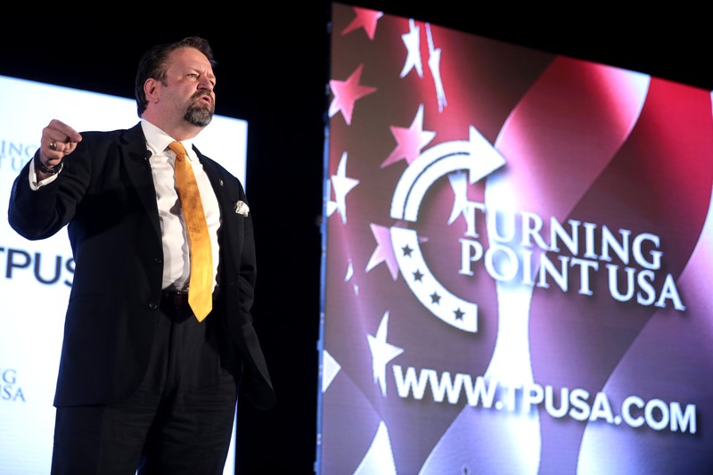 Sebastian Gorka speaking at a political event with a patriotic backdrop