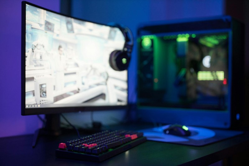 A modern gaming PC setup with a curved monitor displaying a game, RGB-lit keyboard, and ambient purple and blue lighting