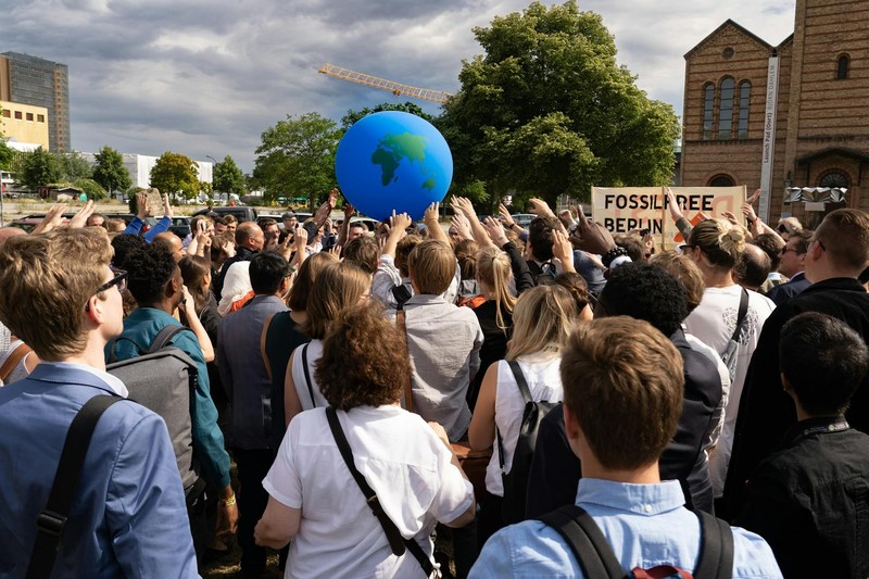 Protesters at a climate rally hold signs reading 'Fossil Free Berlin' and raise a large Earth globe above the crowd