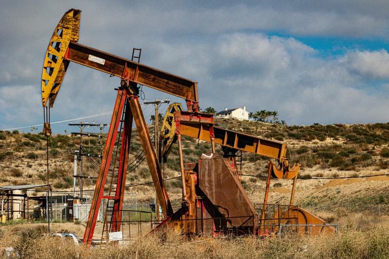 A rusty oil pumpjack in an arid, semi-desert landscape under a partly cloudy sky