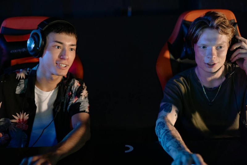 Two gamers engaged in a cooperative gaming session in a dark room with headsets and gaming chairs