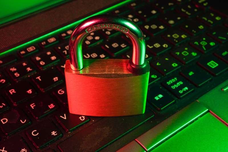 A padlock labeled HARDENED sitting on a laptop keyboard illuminated by green and red lighting