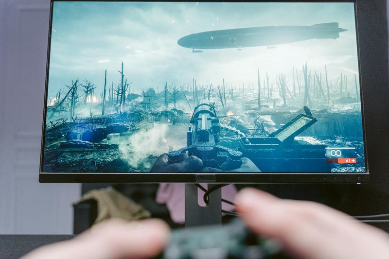 A person's hands holding a game controller while playing a first-person shooter video game on a monitor