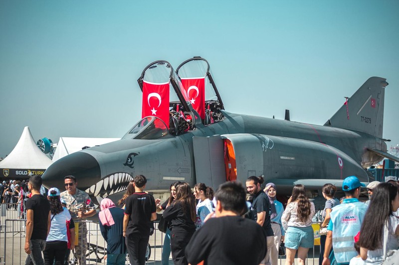 A Turkish Air Force fighter jet on display at Teknofest in Adana, Turkey, with Turkish flags mounted on the cockpit and a crowd of visitors gathered around.