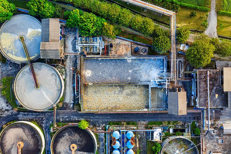 Aerial view of a water treatment facility with large circular processing tanks, rectangular buildings, and extensive piping