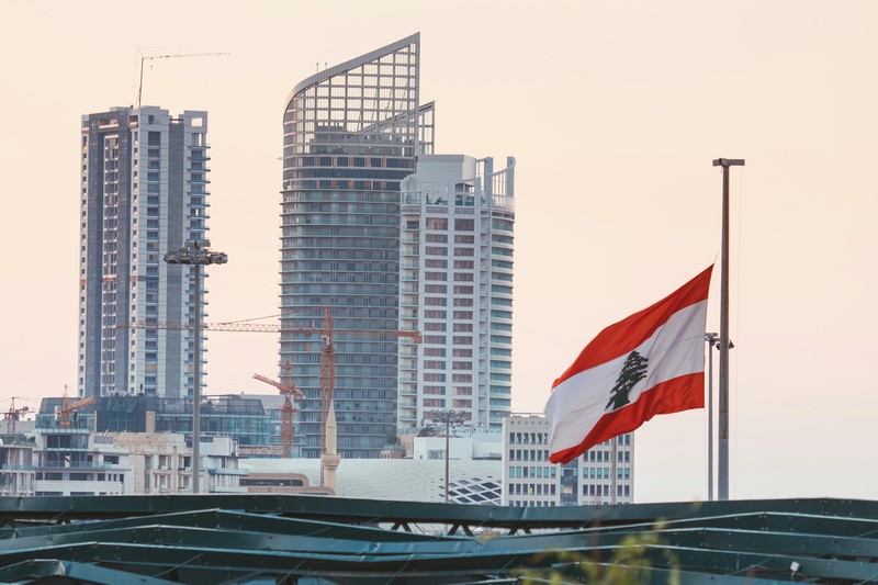Beirut skyline with Lebanese flag waving at sunset, featuring skyscrapers and construction cranes