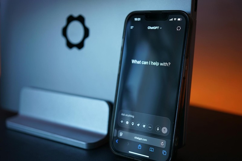 An iPhone displaying the Siri voice assistant interface with the prompt 'What can I help with?' alongside a smart home device on a dark surface with blue and orange ambient lighting.