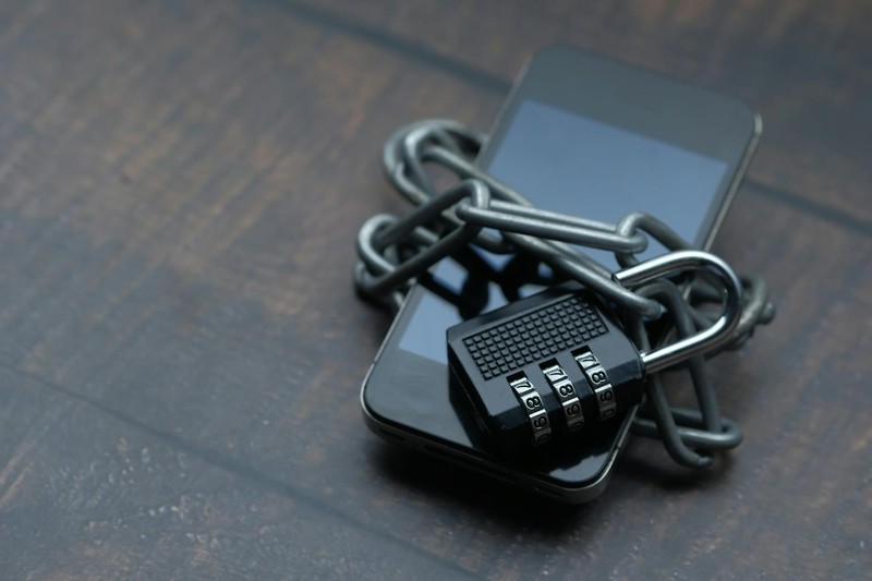 Two smartphones wrapped in a metal chain secured with a combination padlock