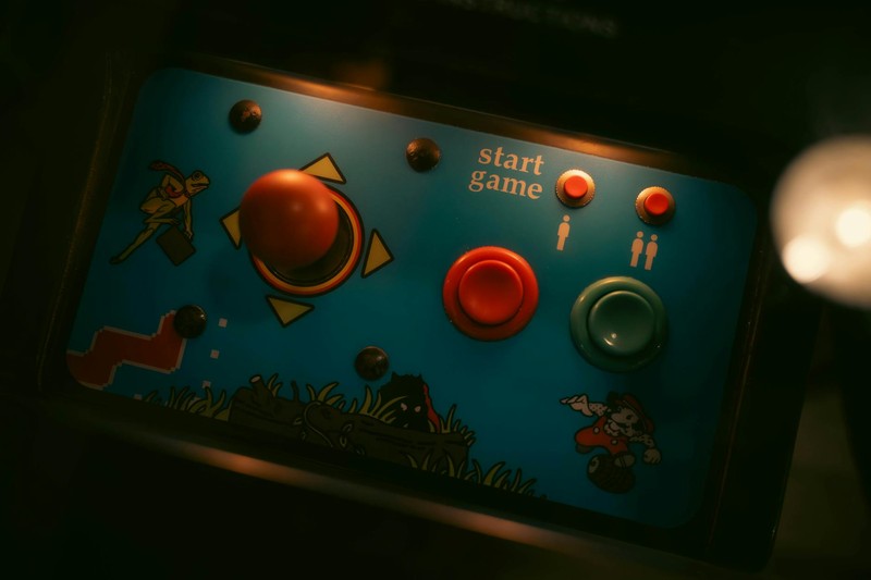 Close-up of a retro arcade game control panel with a red joystick and colorful buttons