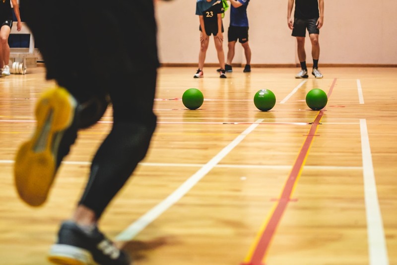Dodgeball game in progress on a polished gymnasium court with green dodgeballs and players