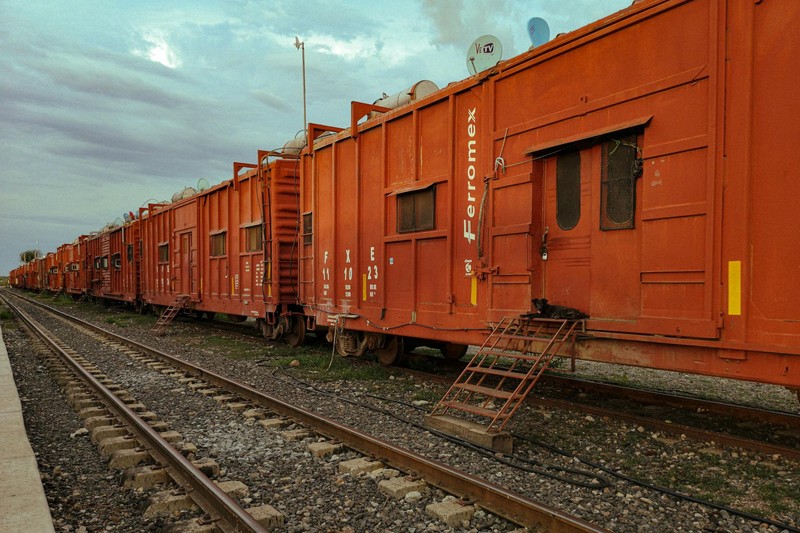 Orange freight boxcars lined up on railroad tracks under an overcast sky