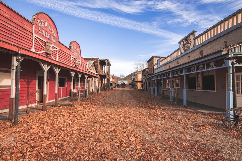 A quiet western town street in autumn with fallen leaves covering the dirt road and vintage buildings