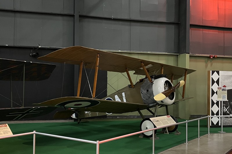 A Sopwith F.1 Camel biplane replica on display in a museum, with British RAF roundels visible on the wings